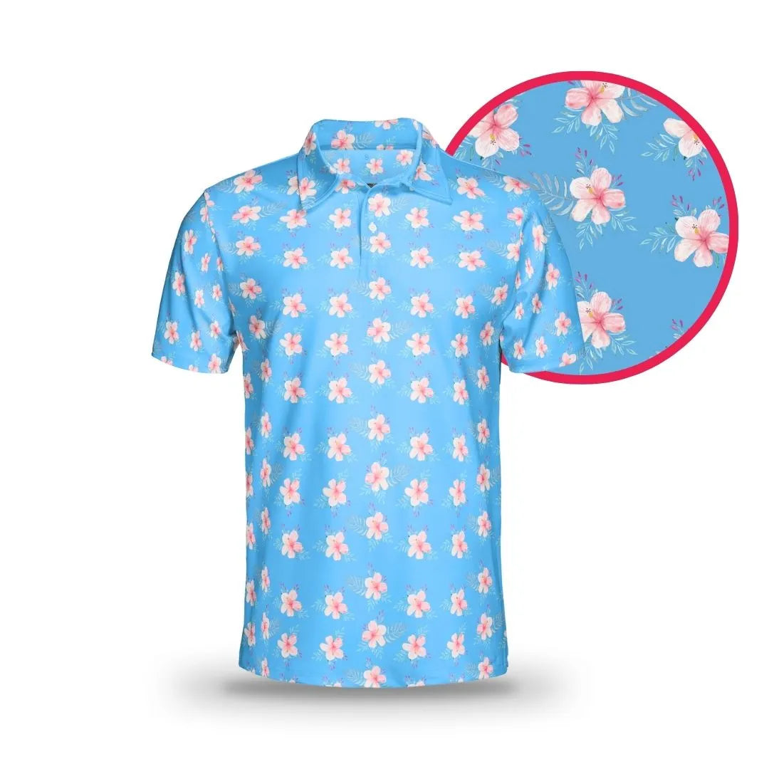The Grunk Dolfer Hibiscus Hitter is a light blue short-sleeve polo featuring a repeating pink hibiscus and green leaf pattern, great for Hawaii or golf. A close-up highlights the detailed floral design on the blue background.