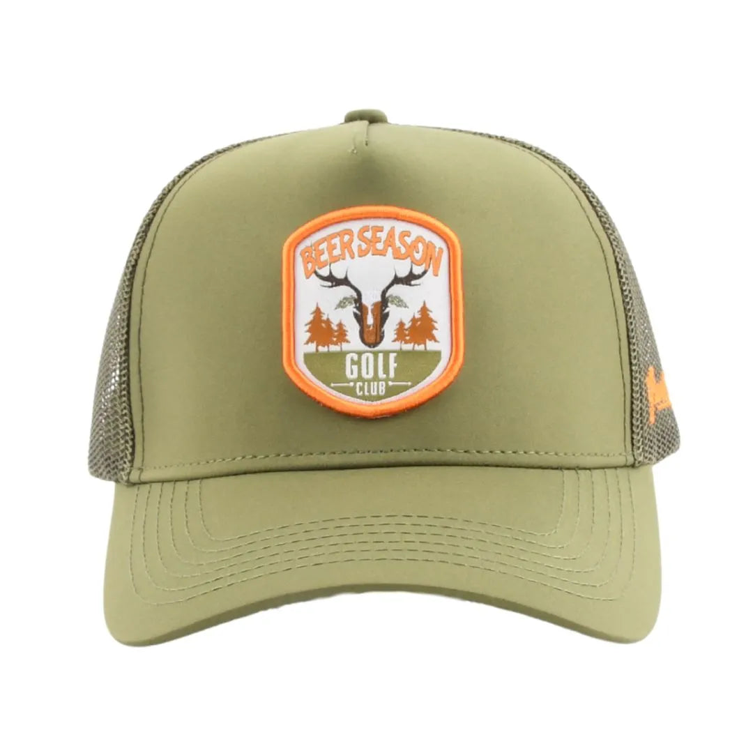 The Grunk Dolfer Beer Season Trucker is an olive green hat with breathable mesh and a front patch showing antlers, pine trees, a golf flag, and the Beer Season Golf Club logo in orange and white.
