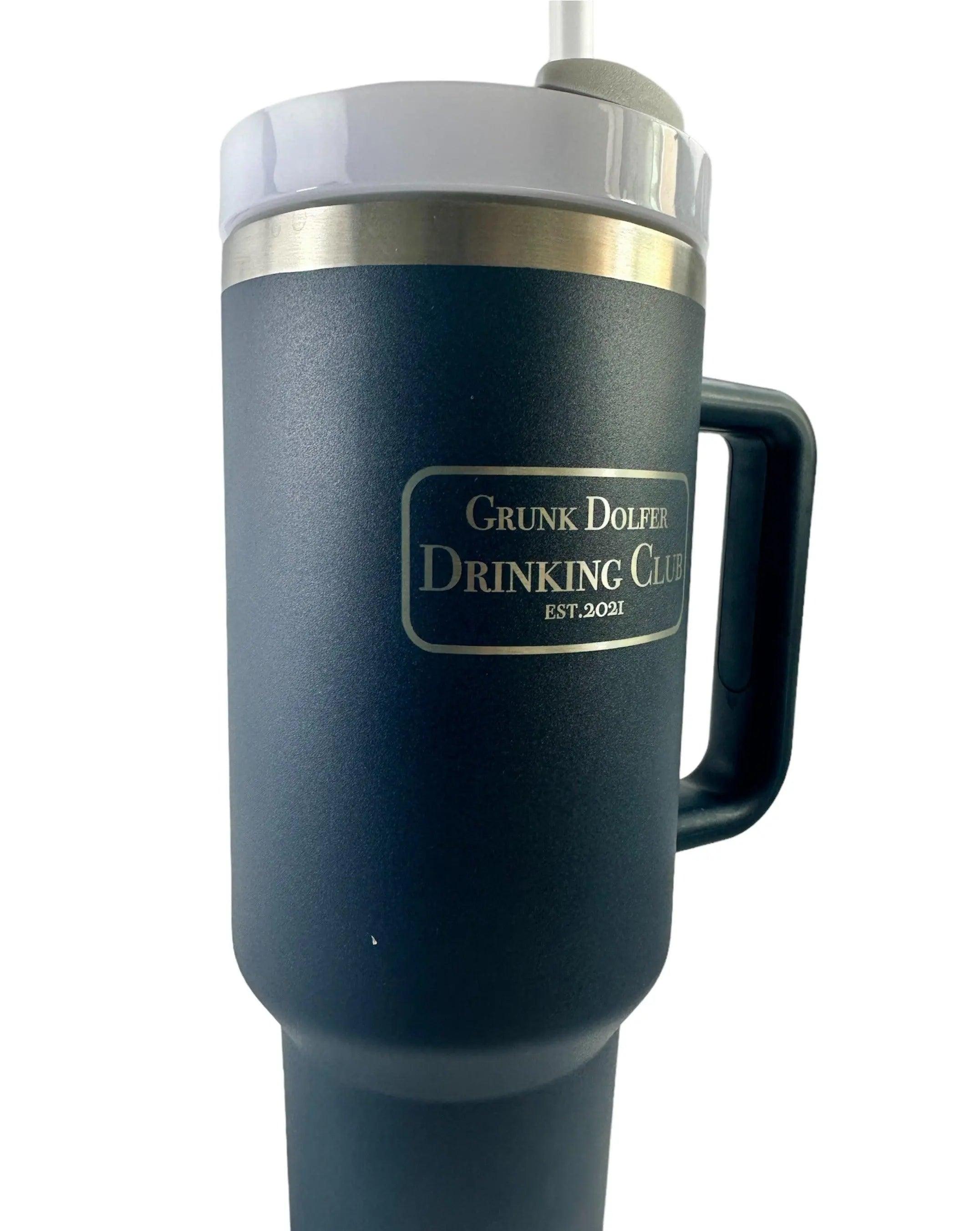 The Manly by Grunk Dolfer is a dark blue golf course tumbler with a handle, white lid, and metal band. It has double wall vacuum insulation and gold lettering: Grunk Dolfer Drinking Club Est. 2021.