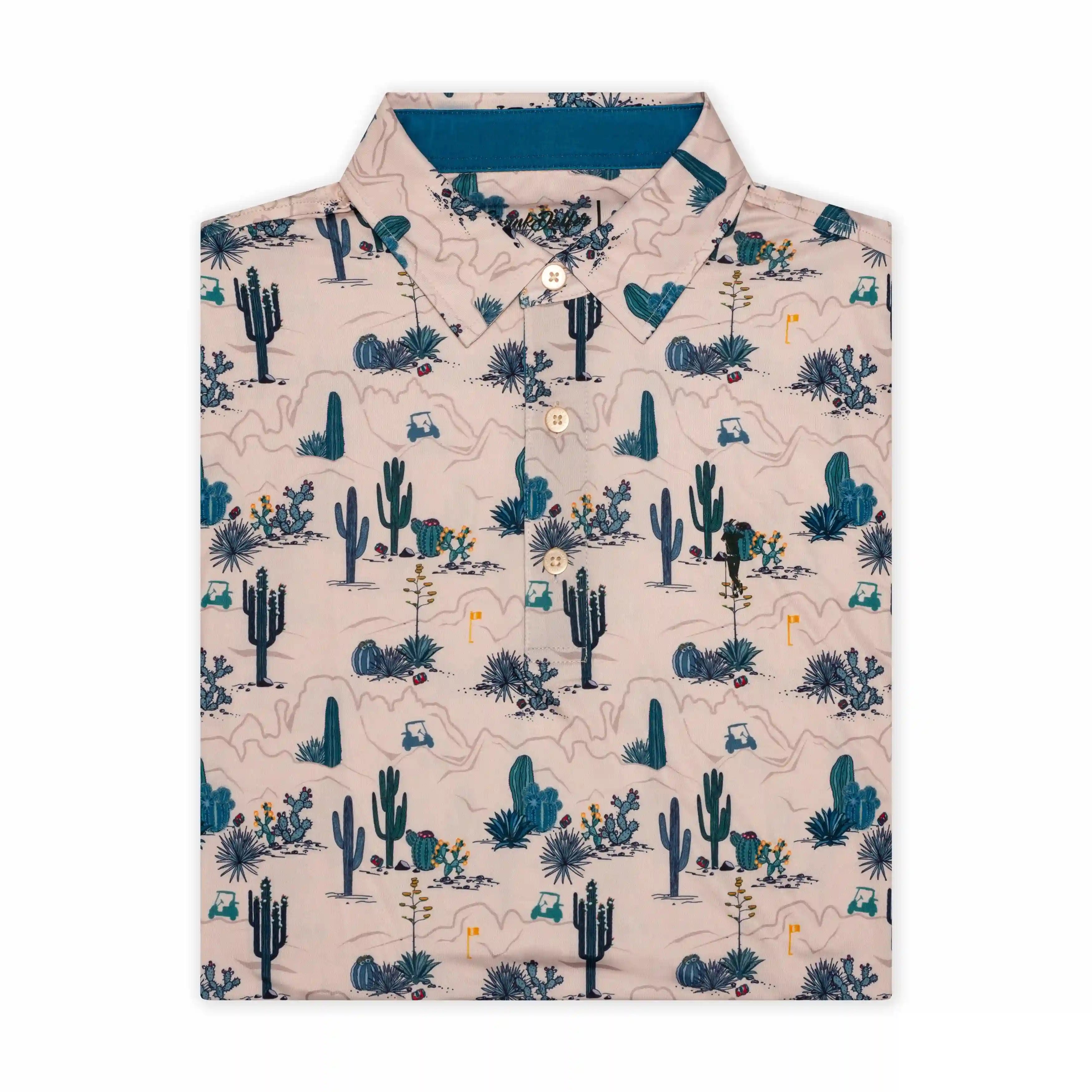 The Grunk Dolfer Desert Classic is a light-colored button-up with a desert-themed print of cacti, rocks, and small animals in blue and green—ideal for a laid-back look or golf apparel.