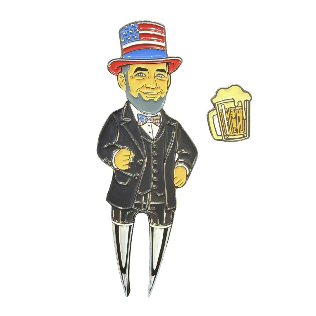 A cartoon Abraham Lincoln in an American flag hat and bow tie stands beside a beer mug, his legs resembling the Grunk Dolfer Lincoln Divot Tool—premium metal, also a magnetic ball marker.