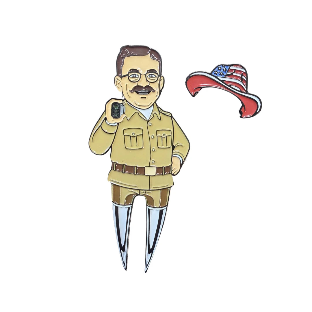 The Grunk Dolfer Teddy Divot Tool is a pin of a cartoon man in a tan uniform with glasses, mustache, and walkie-talkie beside an American flag red cowboy hat; the bottom half forms a divot tool with two metal prongs.