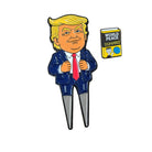 A cartoon figure in a suit with yellow hair stands beside a small illustrated book titled World Peace for Dummies, featuring a yellow cover and a small owl drawing, while holding the Grunk Dolfer Trump Divot Tool with magnetic ball marker—a must-have accessory for any golf enthusiast looking to repair divots in style.