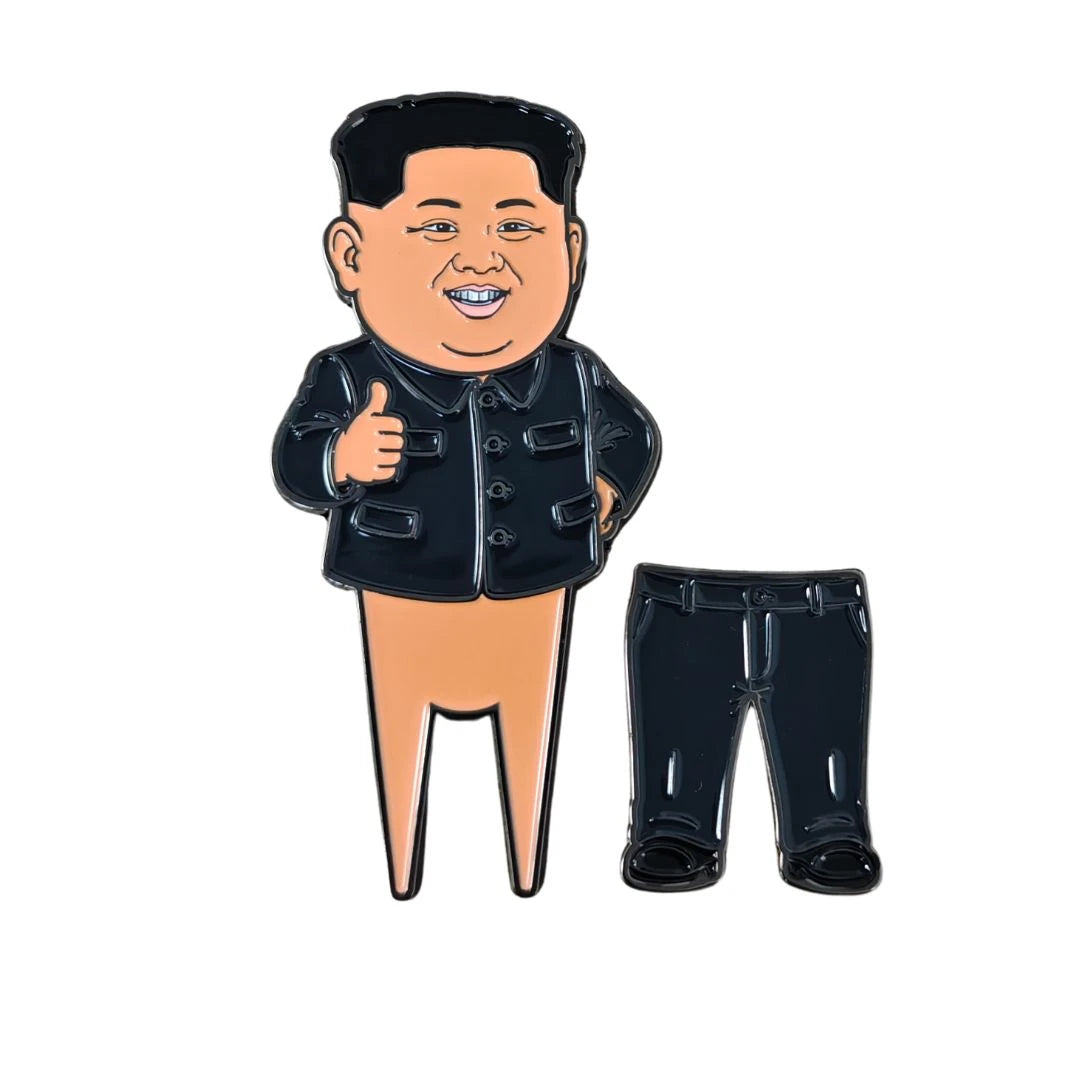 Showcasing Grunk Dolfer’s “Kim Jong Divot Tool,” this quirky set features a cartoon pin of a smiling man with no pants giving a thumbs-up, playfully paired with a separate pin of black pants. A fun twist on the classic golf divot tool or magnetic ball marker, it’s the perfect gift for golf enthusiasts. White background.