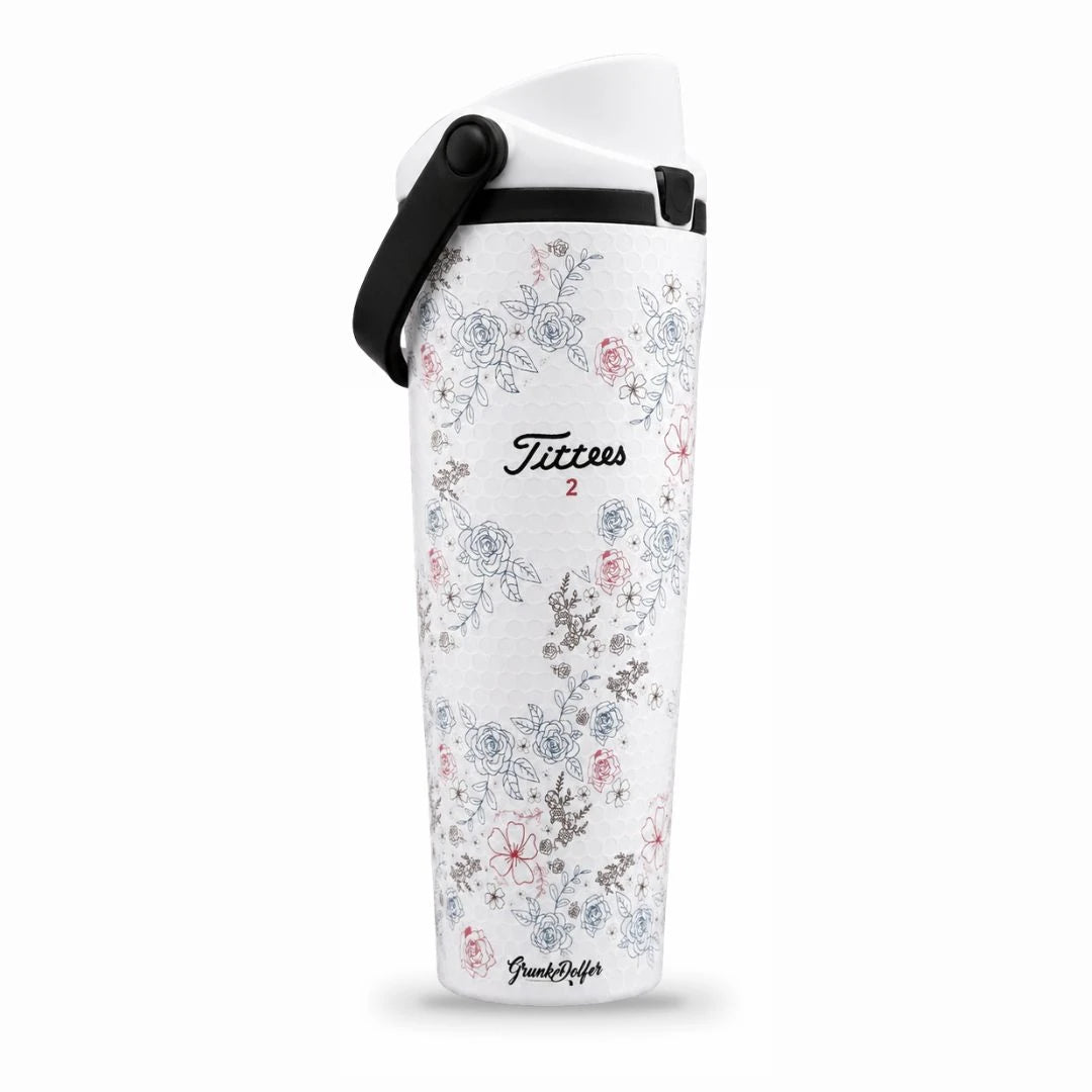A white travel mug with a black handle, decorated with blue, grey, and pink floral designs. The front features the product name Tittees Growler and the number 2, along with a small Grunk Dolfer logo at the bottom. Perfectly sized for your favorite drinks on the go, this mug blends style and function—making it an ideal alternative to a stainless steel hydration bottle or 32 oz container.