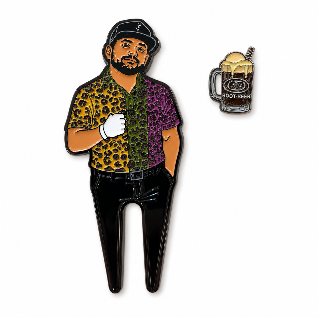 An illustrated enamel pin features a man in a leopard print shirt, cap, and glove standing with one hand in his pocket, looking ready for the fairway with Grunk Dolfer’s The Mod Goat Divot Tool at his side. Beside him is a small pin of a root beer float served in a mug labeled “Root Beer.”.